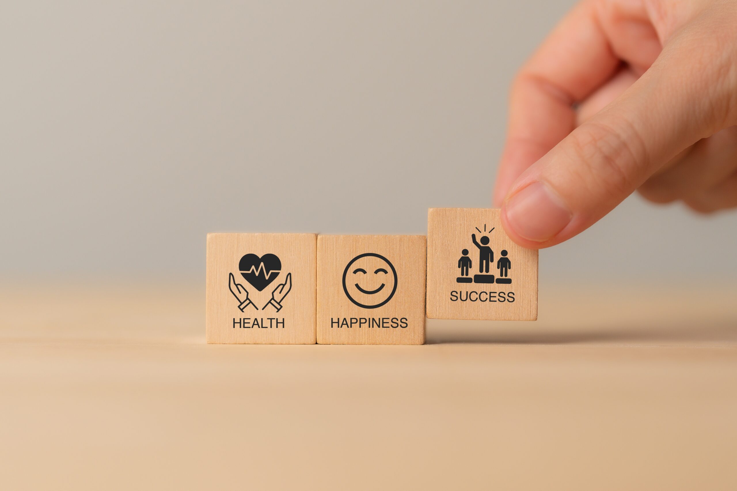 Close-up of a hand arranging wooden blocks with icons and words representing health, happiness, and success